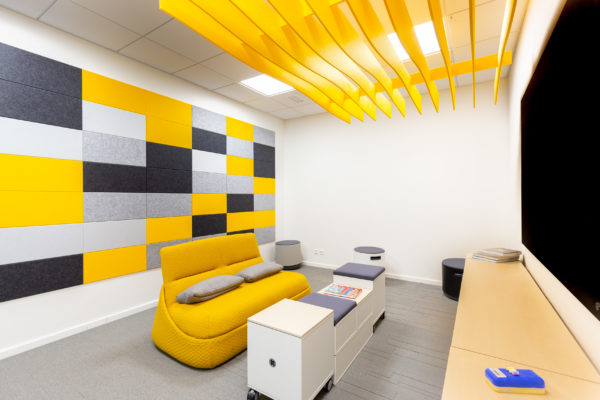Toimiston kattorakenteisiin ja seiniin asennettu design-akustiikka, jossa keltaisia, mustia, valkoisia ja harmaita elementtejä.